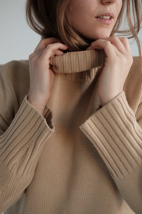 Crop gentle female with long hair wearing warm beige sweater in white studio