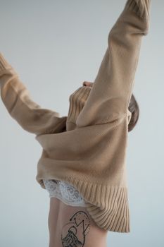 Side view of unrecognizable female model raising hands while putting on soft turtleneck to gray background