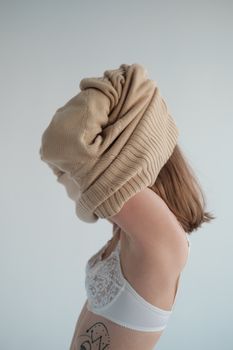 Side view of unrecognizable female model in bra putting on soft turtleneck against gray background