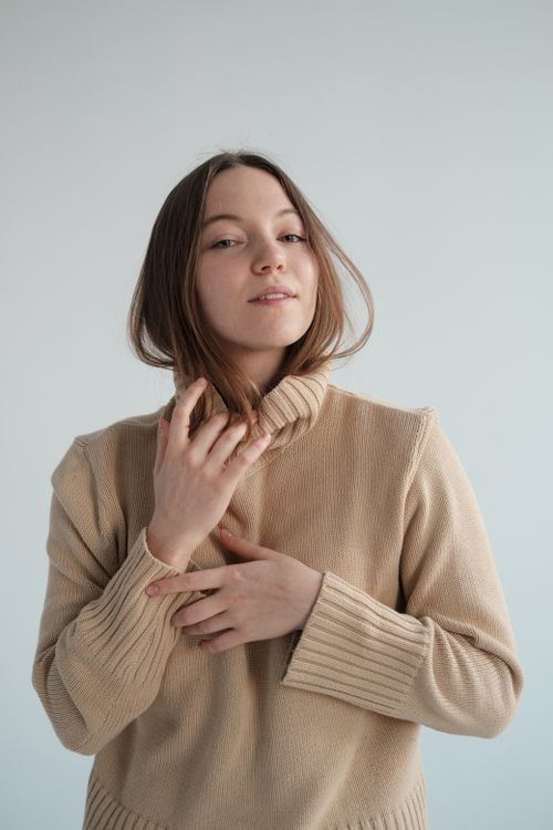 Free Charming female with long hair gently touching soft turtleneck and looking at camera against gray background Stock Photo