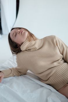 High angle of sleepy young female with closed eyes wearing turtleneck leaning on hand while lying on floor