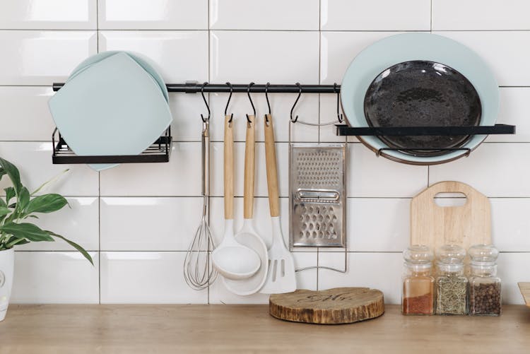 Plates And Utensils On White Wall And Spices On Wooden Surface