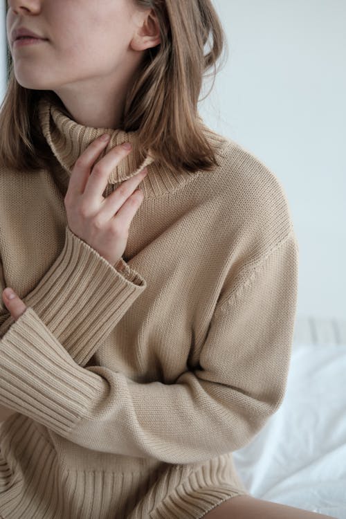 Free Peaceful female wearing soft sweater sitting on bed with crossed arms and looking away Stock Photo