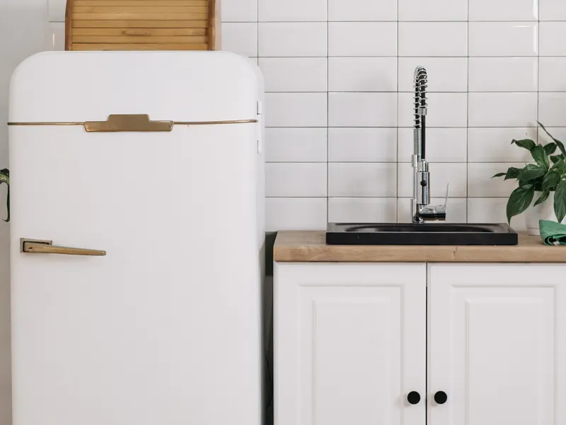 Vintage white fridge beside a kitchen sink with condenser coils at the bottom Vintage white fridge beside a kitchen sink with condenser coils at the bottom