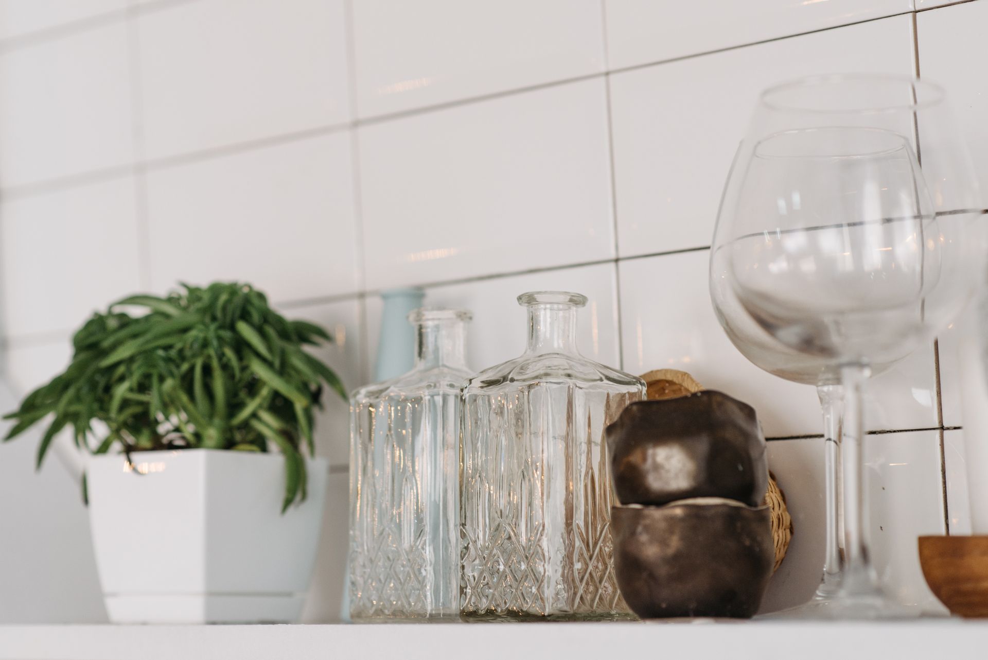 A modern kitchen shelf showcasing glassware and a lush potted plant against a tiled wall.