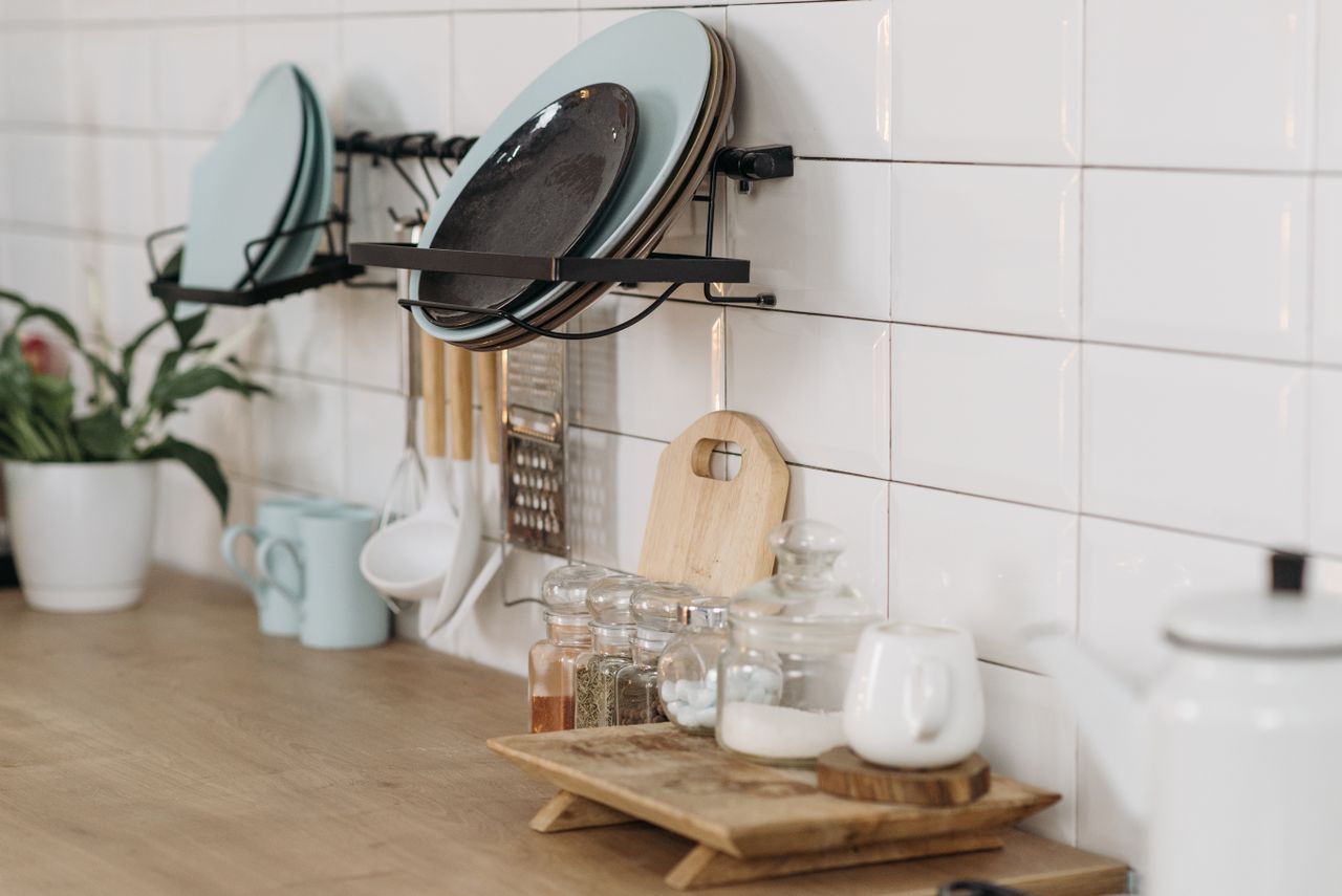 Wall-mounted black metal plate rack holding plates above a kitchen counter with spice jars