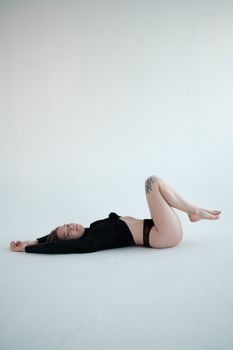 Side view full body slender female in black sweater and panties lying on back on floor in light studio and looking at camera