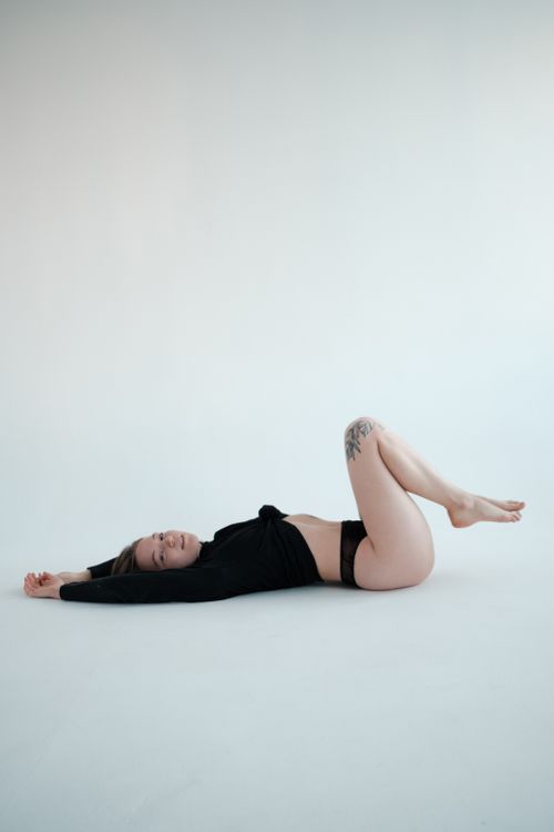 Free Side view full body slender female in black sweater and panties lying on back on floor in light studio and looking at camera Stock Photo