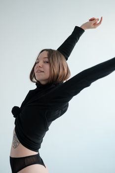 Side view of positive woman in black underwear and long sleeve shirt standing in studio against white background and looking at camera