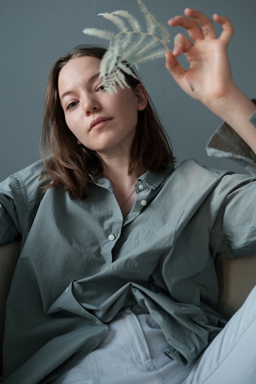 Young woman sitting on couch with branch of plant