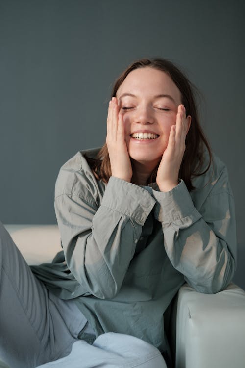 Free Smiling woman sitting on sofa and gently embracing cheeks Stock Photo