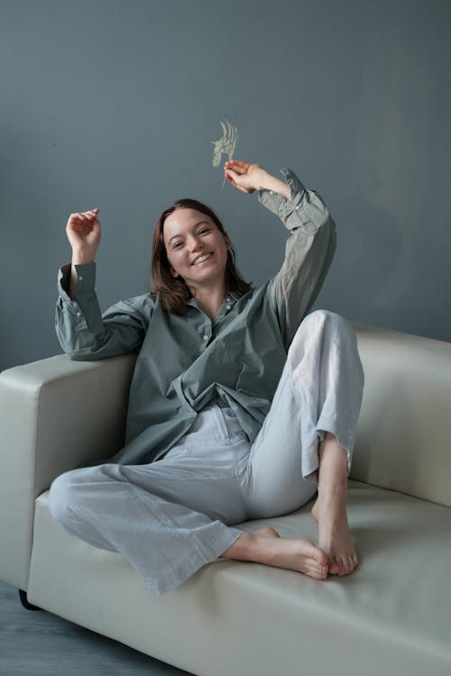 Cheerful woman with branch of plant sitting on sofa