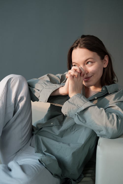 Positive woman with folded hands sitting on sofa