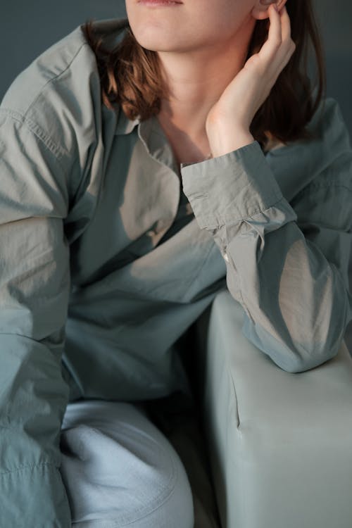 High angle of crop faceless female wearing casual linen shirt and pants sitting on couch