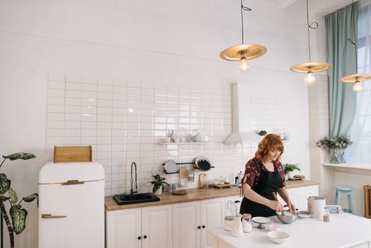 Redheaded woman in apron baking, surrounded by modern kitchen decor.