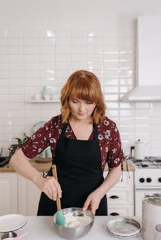 Woman in apron preparing food with focus on kitchen activity.