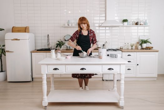 Woman baking in a bright, modern kitchen with white cabinets and appliances.