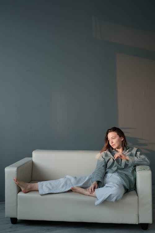 Free Full body of serene barefoot female resting on sofa in sunlight and looking away Stock Photo