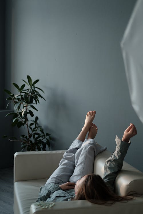 Full body of barefoot female with hand up chilling on couch placed near potted plant