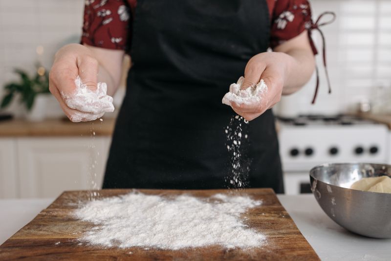 Hands sprinkling flour on a chopping board