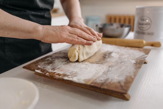 Hands kneading dough on a floured wooden board, in a warm kitchen setting.