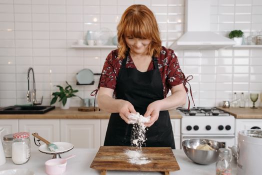 Woman wearing apron kneading dough in a modern kitchen while smiling, enjoying the baking process.