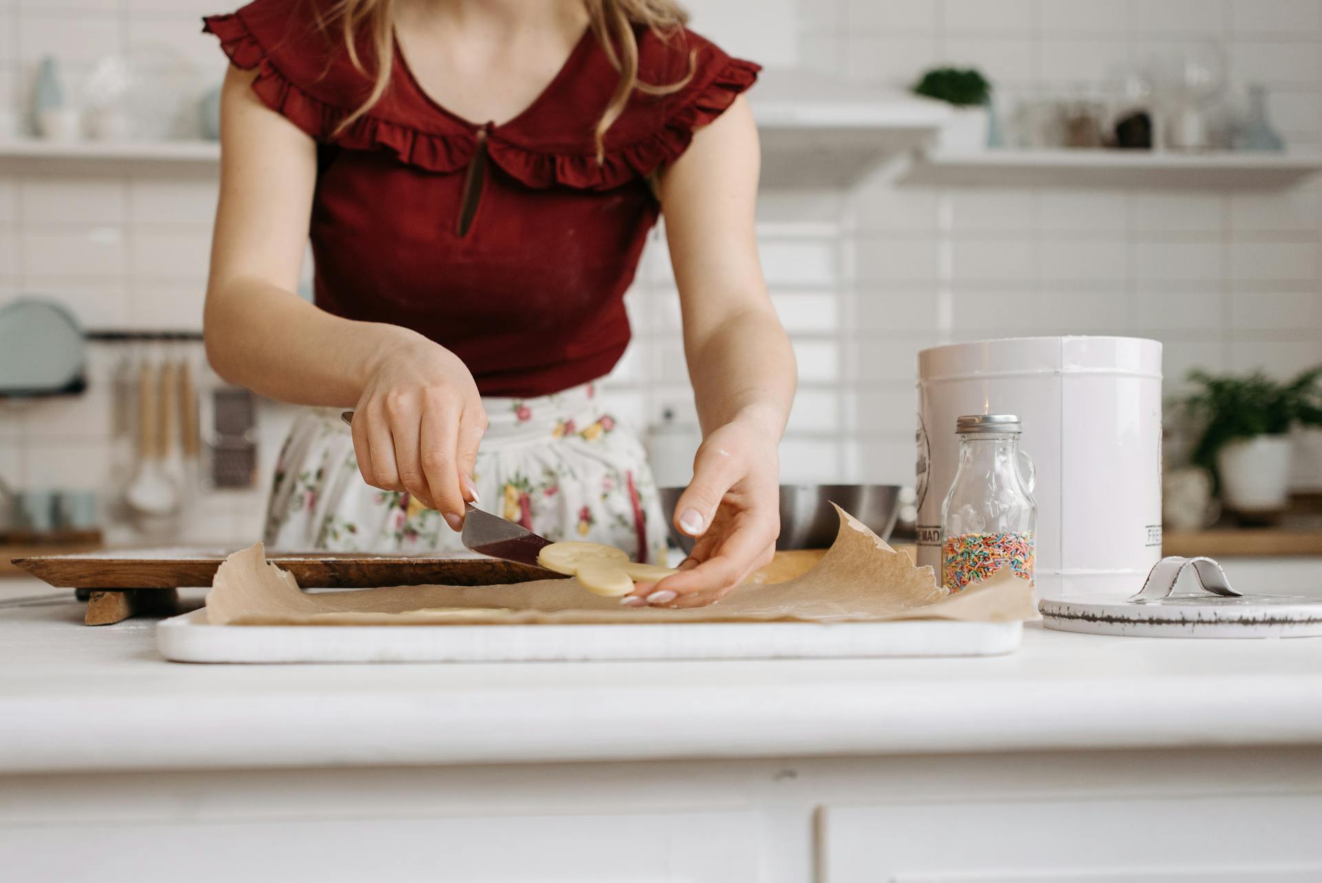 Woman's hands placing cookie dough on parchment paper in a cozy kitchen.