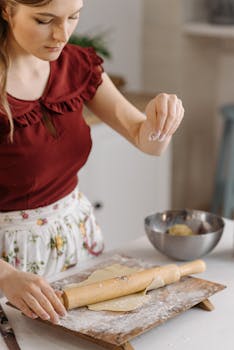 Woman kneading dough on a wooden board with a rolling pin and flour in an indoor kitchen setting.