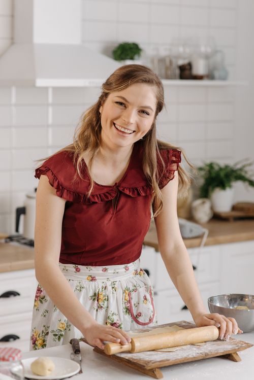 Free A cheerful woman uses a rolling pin on a dough board in a bright kitchen setting. Stock Photo