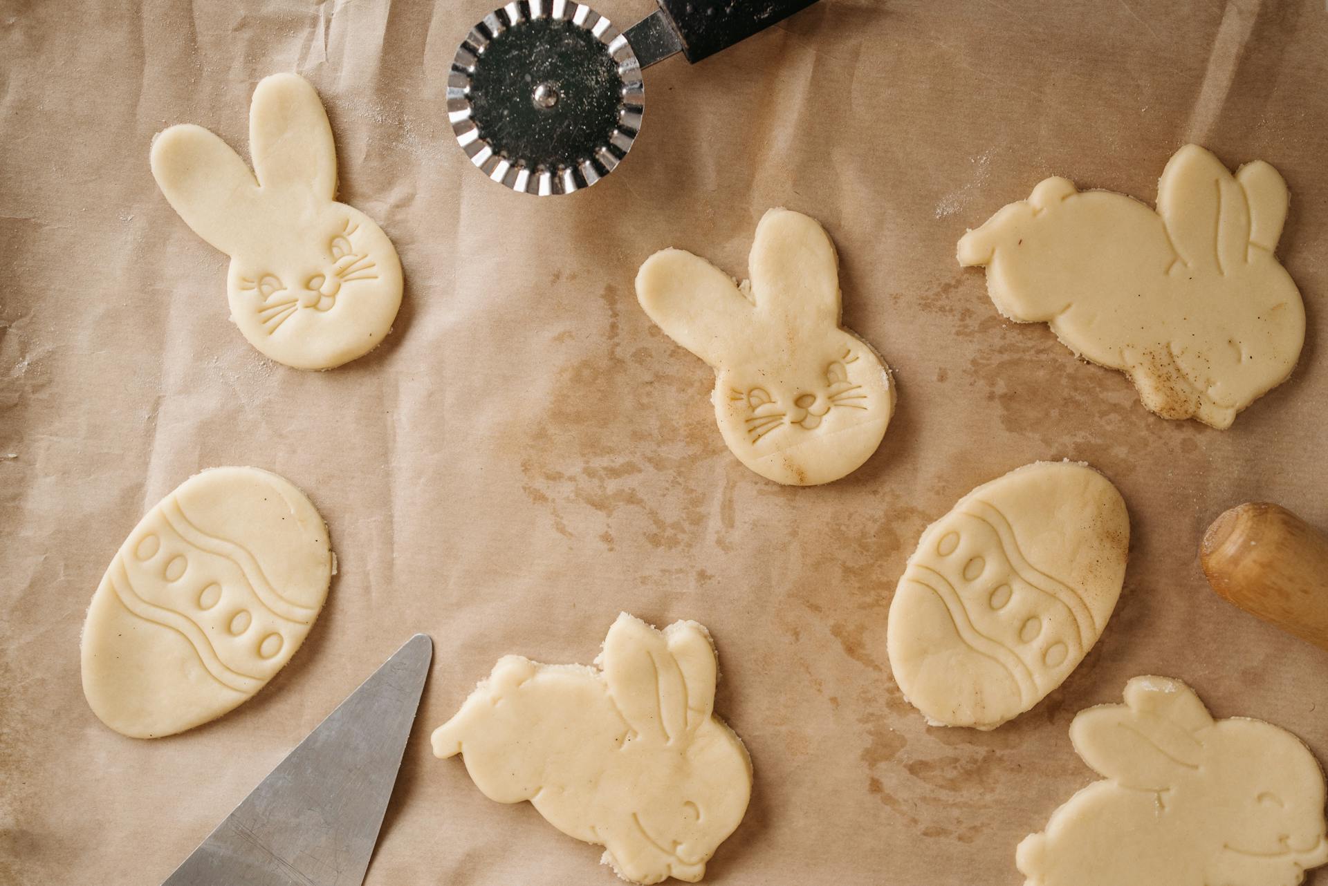 Easter-themed sugar cookie cutouts shaped as bunnies and eggs on parchment paper.