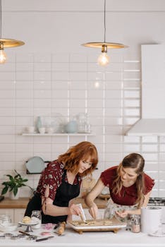 Two women baking together in a bright, modern kitchen setting with white tiles.