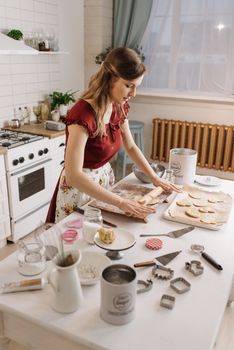 A woman rolling dough to make homemade cookies in a cozy kitchen setting with various baking tools.