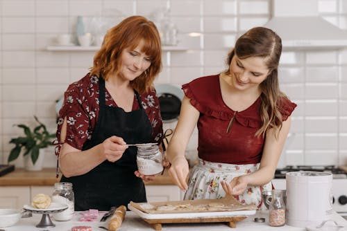 Two women joyfully baking cookies together in a cozy kitchen setting, capturing a warm family moment.