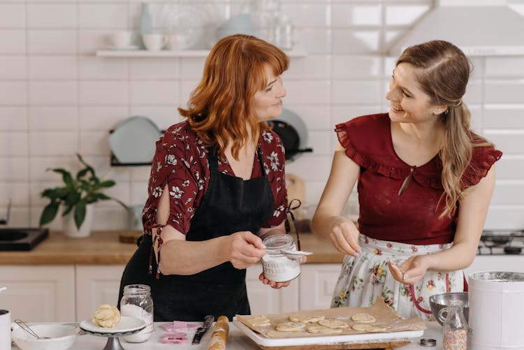 A Woman In Black Apron Holding A Jar Of Sugar In The Kitchen While Baking