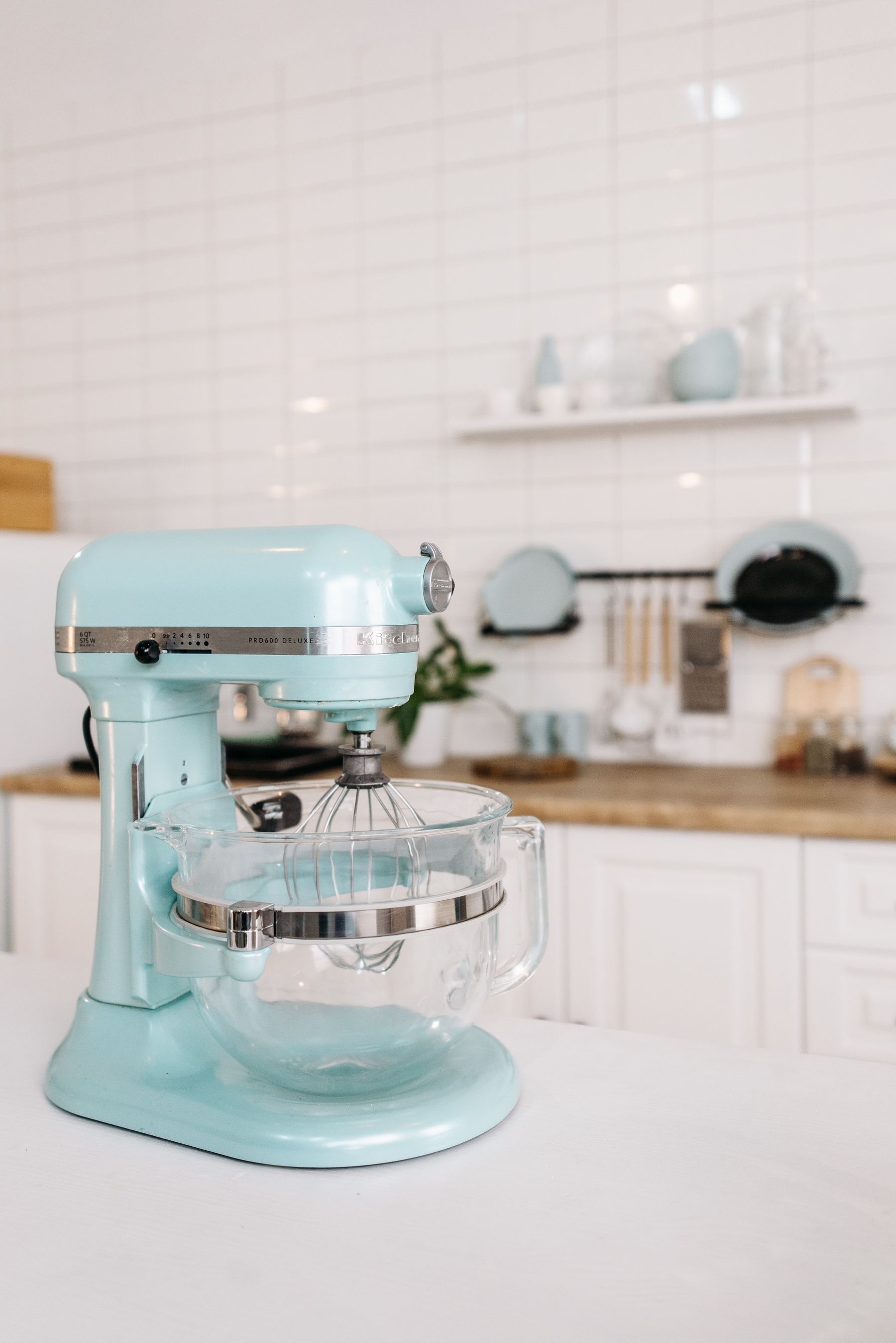 A mint green stand mixer with a glass bowl prepared for baking in a bright white kitchen