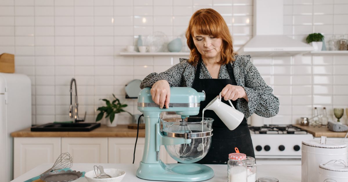 A woman pouring milk into a pale blue stand mixer