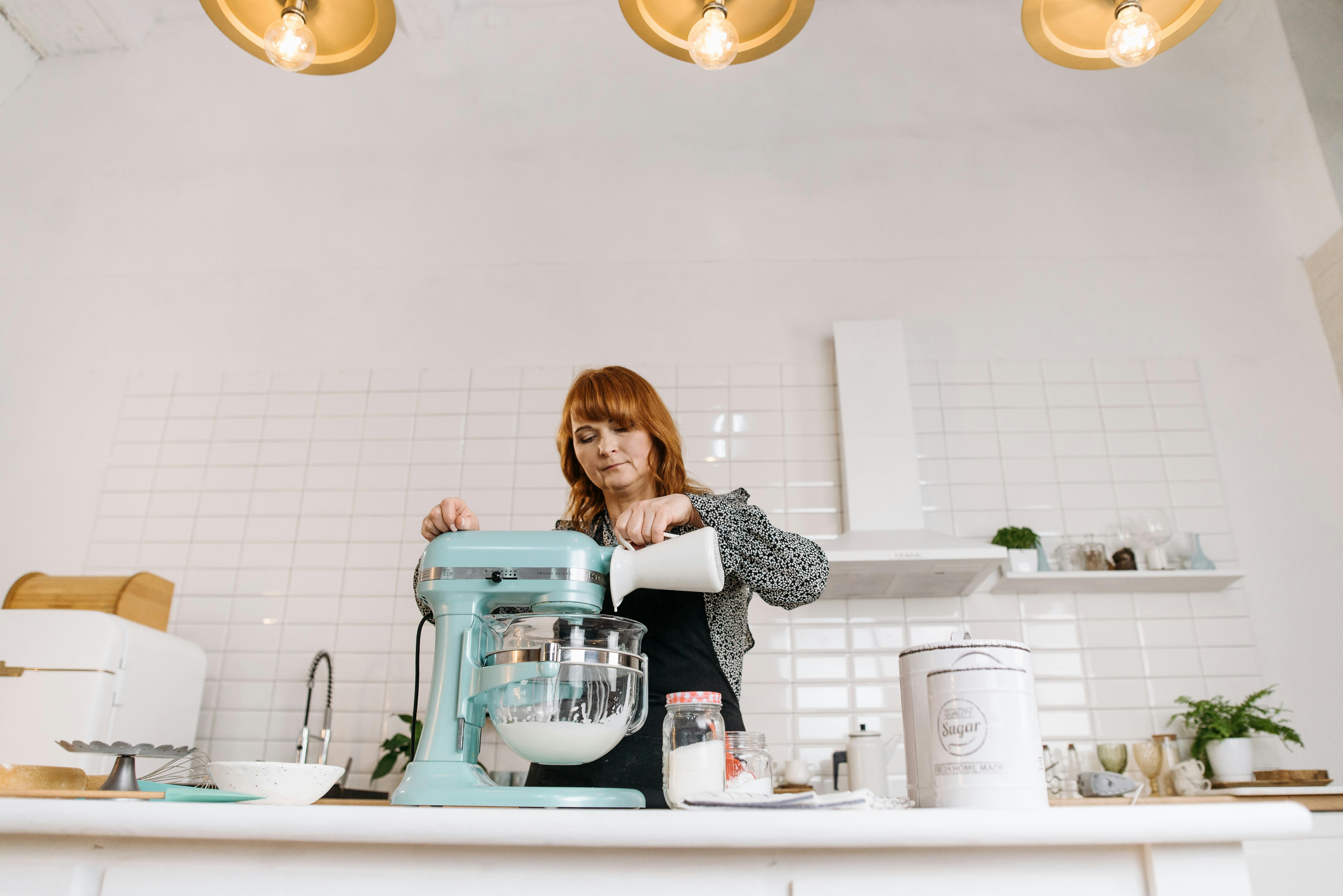 Woman pouring milk into a stand mixer while baking in a stylish kitchen.
