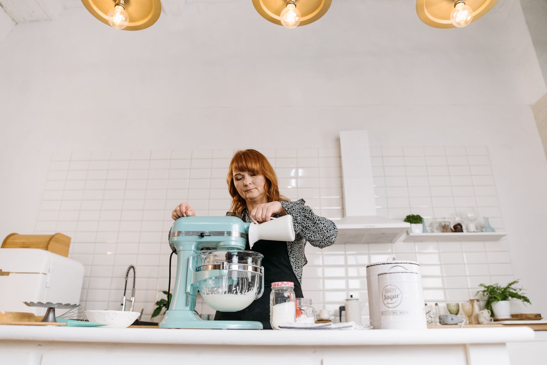 Woman pouring milk into a stand mixer while baking in a stylish kitchen.