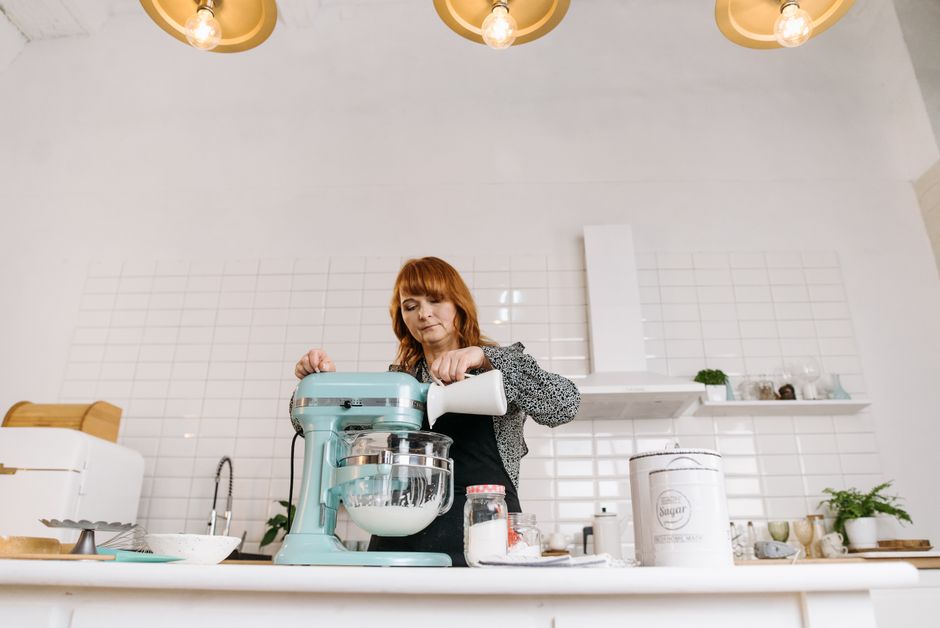 Woman pouring milk into a stand mixer while baking in a stylish kitchen.
