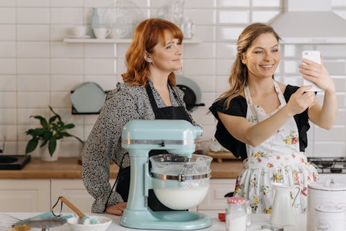 Free Woman Taking a Picture of Her and Another Woman While Baking in the Kitchen  Stock Photo