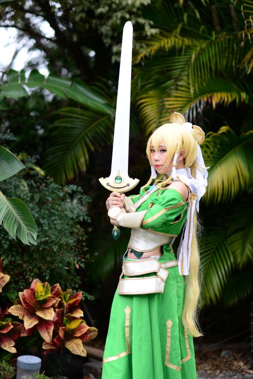 Free Cosplayer in a green costume poses as a fantasy warrior with a sword outdoors. Stock Photo