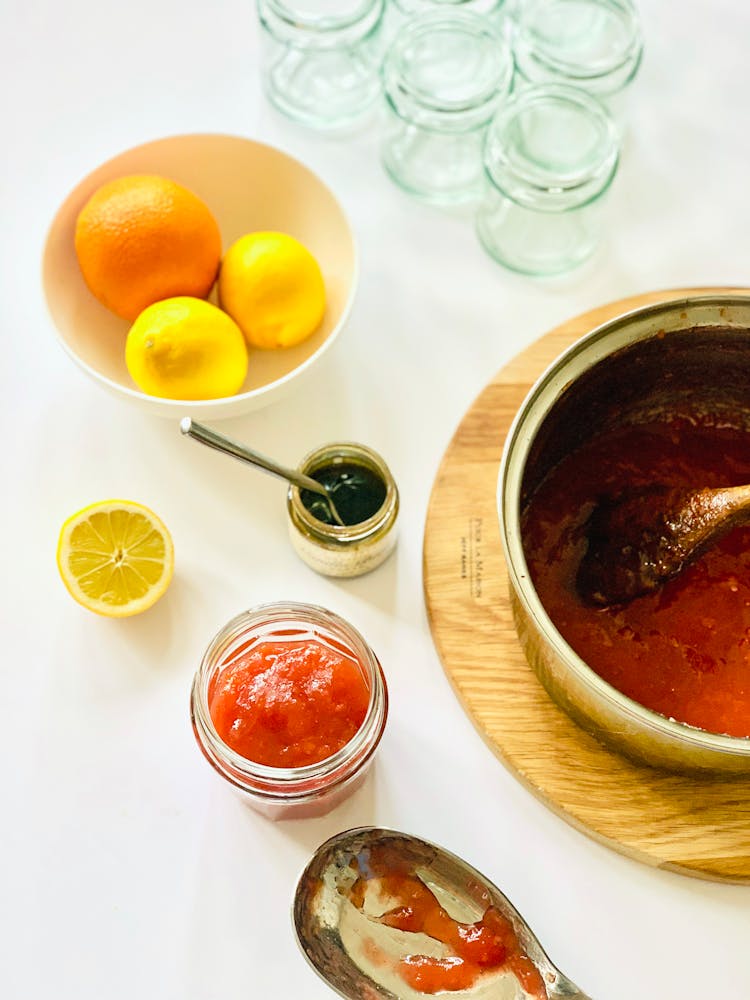 A Bowl Of Citrus Fruits And Jams On White Table