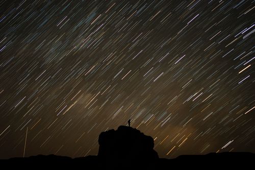 Free A stunning time-lapse of star trails over a rock silhouette at night. Stock Photo