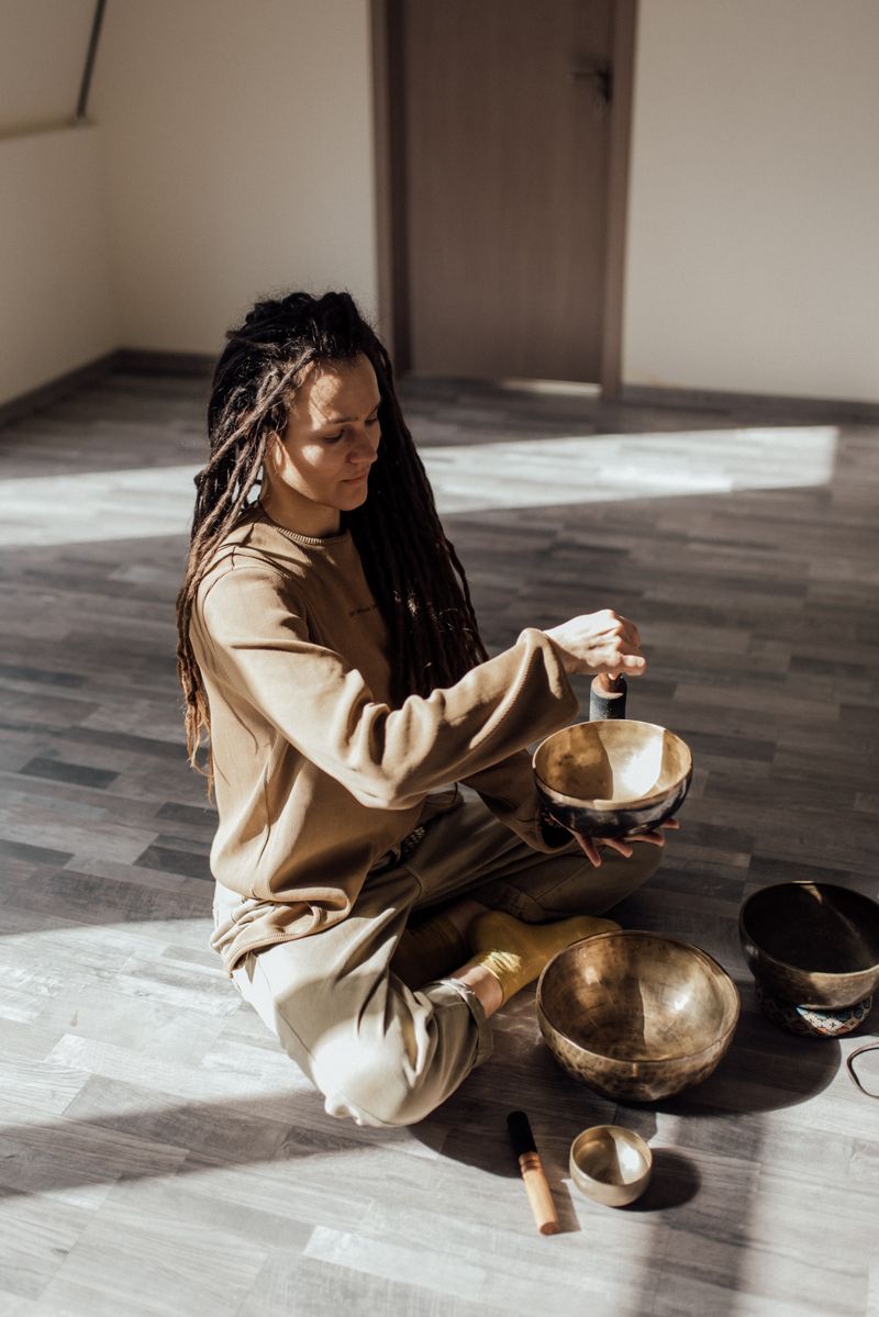 Woman meditating indoors with Tibetan singing bowls, promoting relaxation and mindfulness.