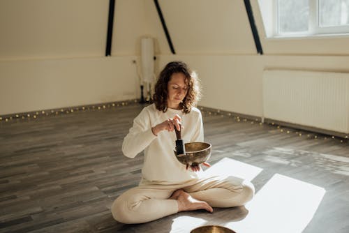 Free 
A Woman Using a Tibetan Singing Bowl while Sitting on the Floor Stock Photo