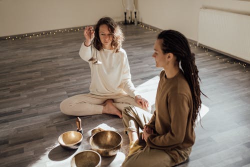Free Women Meditating with Tibetan Singing Bowls while Sitting on the Floor Stock Photo