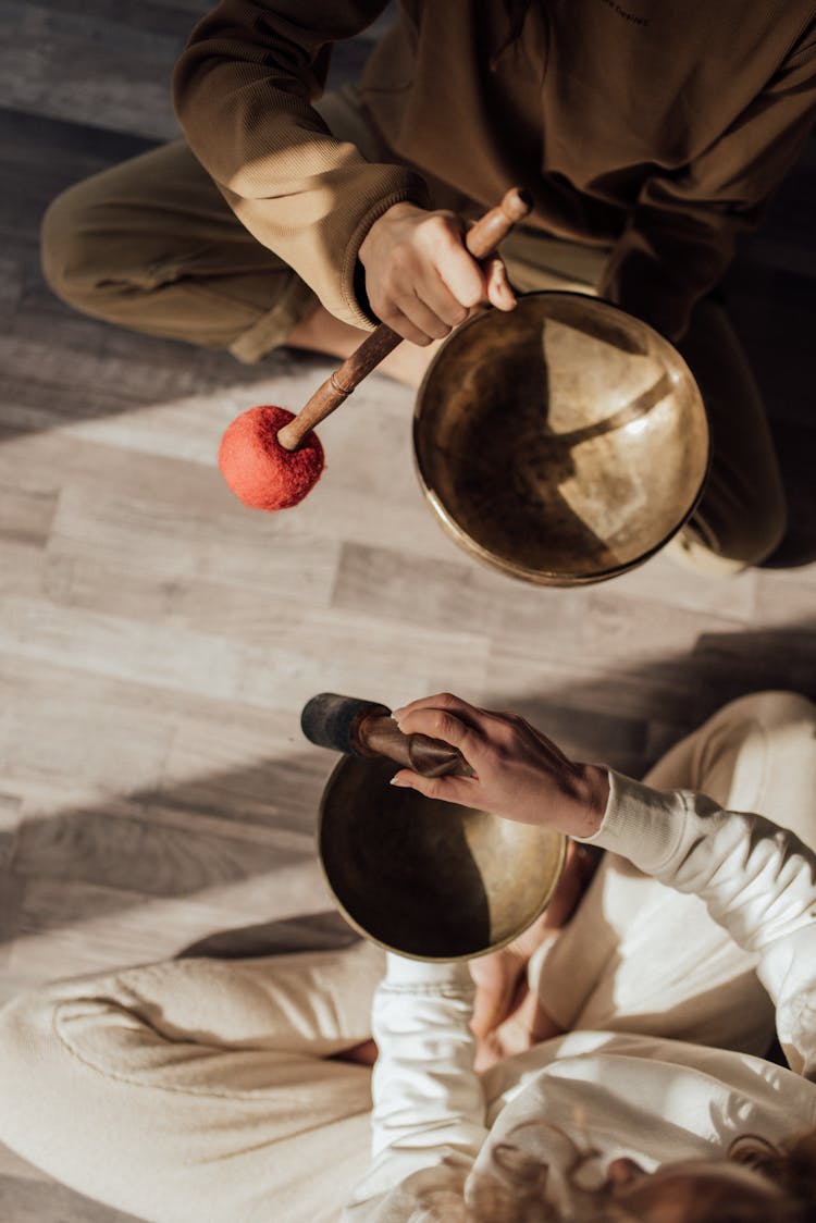 Two People Sitting On Floor Using Tibetan Singing Bowls