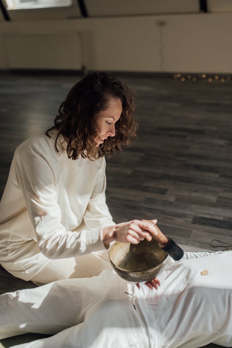 A Woman Holding A Mallet And Singing Bowl Over A Person