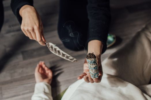 Hands using a feather and smudge stick in a spiritual ritual, symbolizing purification and meditation.