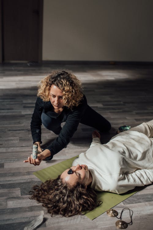 A Woman Holding White Sage Near a Woman Lying on Floor 